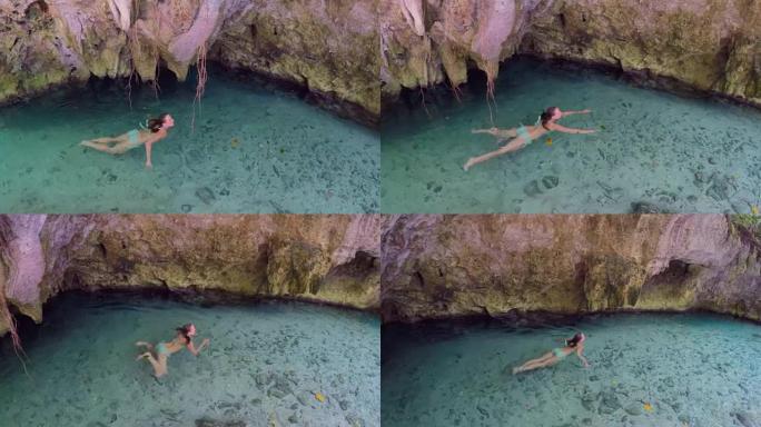 特写: 女人沿着cenote的岩石墙在清澈的河中游泳