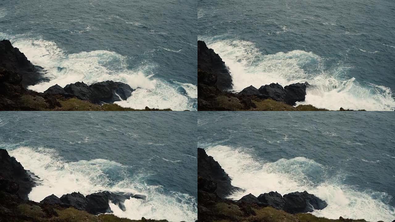 晴天的蓝海海岸特写。波浪溅到黑色的岩石上