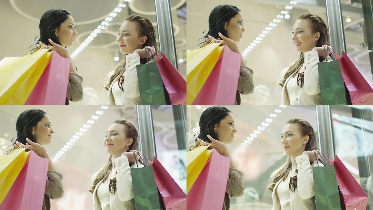 两个快乐微笑的女孩在购物中心有对话电梯