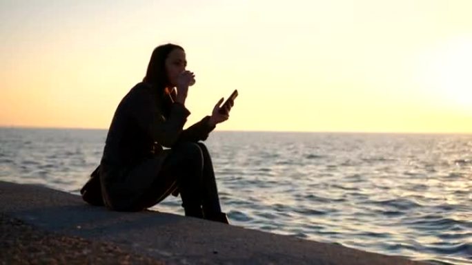 女人在海边日落时检查短信