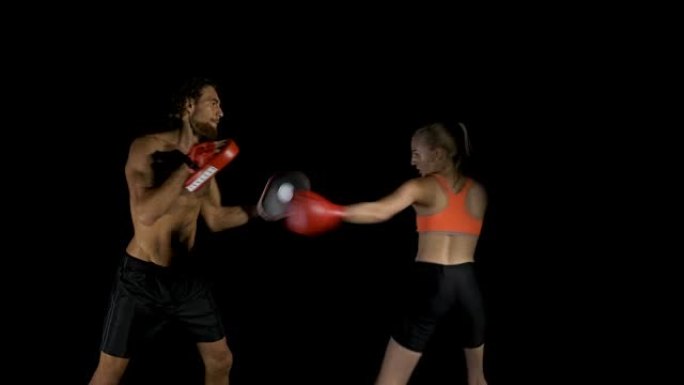 女人在黑色背景下和教练一起练习拳击。
