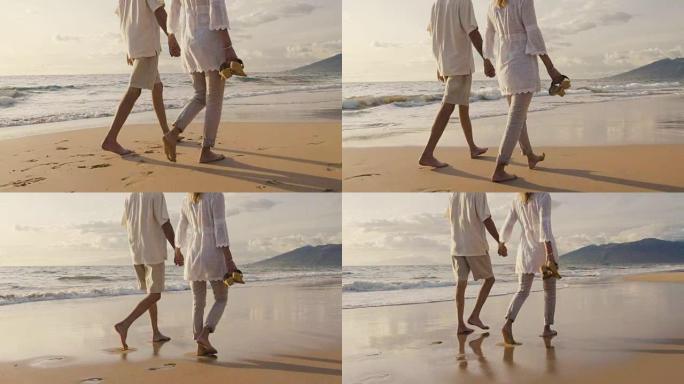 年长的夫妇牵着手，在日落时走在海滩上，弄湿了脚