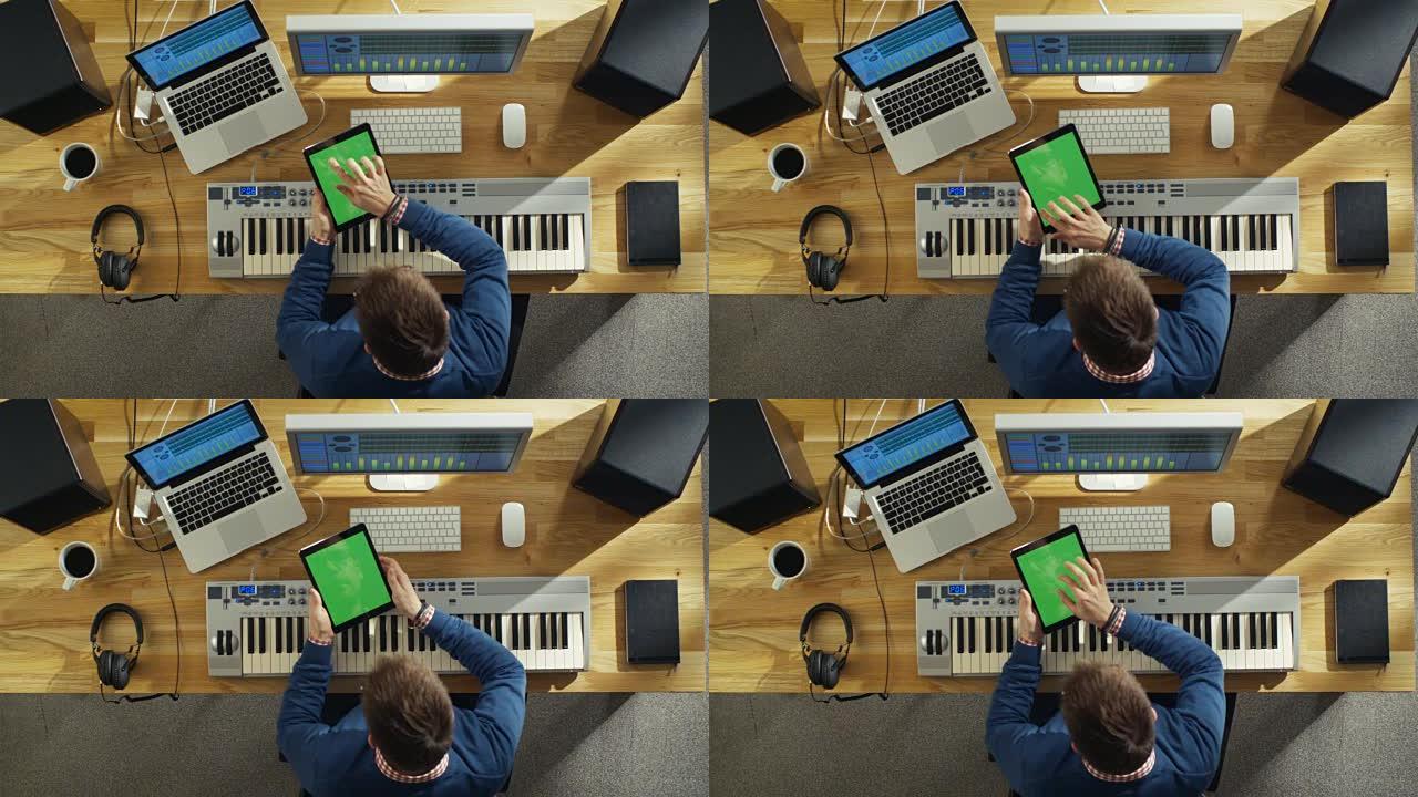 一位音乐家在工作室工作时手持绿色屏幕平板电脑的俯视图。他的工作空间是高科技的，但看起来阳光又温暖。