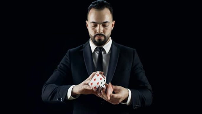 穿着黑色西装的专业魔术师表演手牌技巧。背景是黑色的。