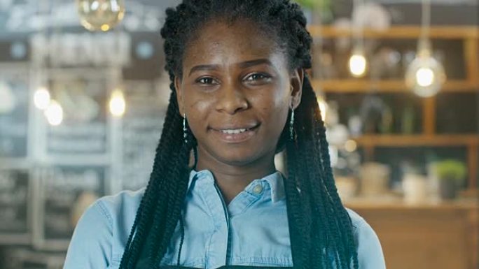 美丽的非洲裔美国咖啡馆老板走进焦点，而在背景中她的时尚的咖啡馆闪耀着灯光。