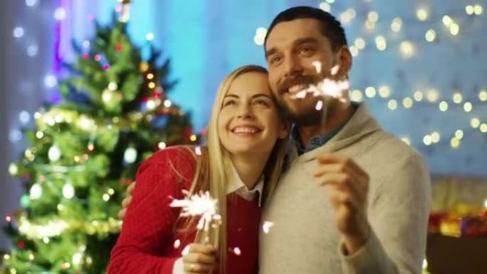幸福的夫妇点燃火花和微笑。背景圣诞树和装饰有灯的房间。