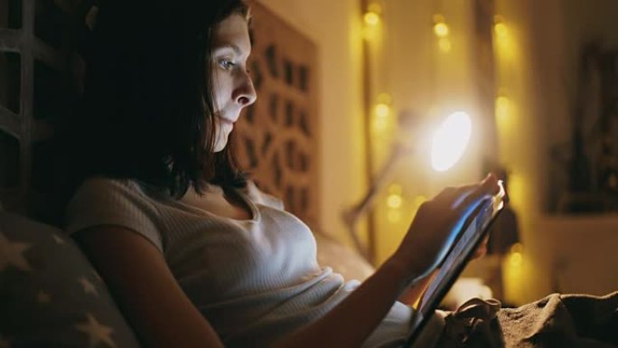 年轻集中的女人使用平板电脑和晚上躺在床上看在线新闻的特写