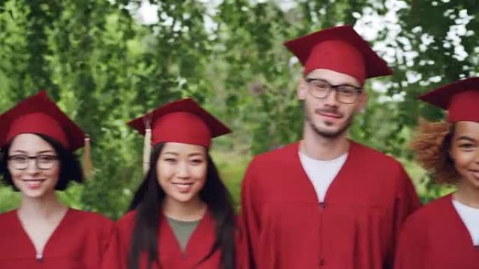 穿着红色毕业礼服和灰泥板站在户外，微笑着看着相机的跨国学生团体的肖像。