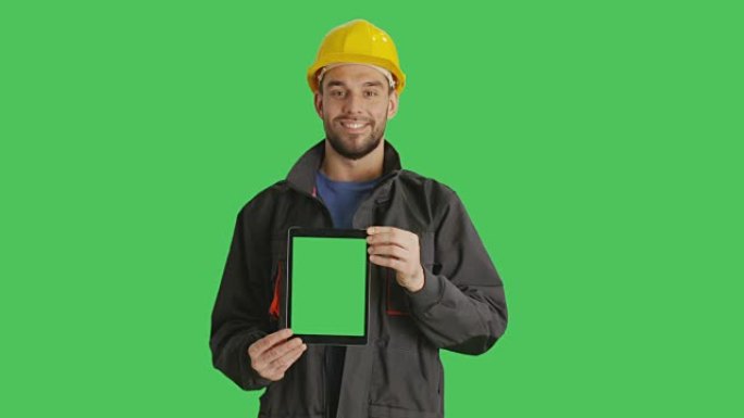 微笑着戴着安全帽的镜头，拿着绿色屏幕的垂直平板电脑。背景中的绿色屏幕。