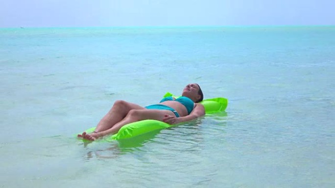 特写: 放松的年轻女子躺在异国情调的岛屿波拉波拉的充气水上床上
