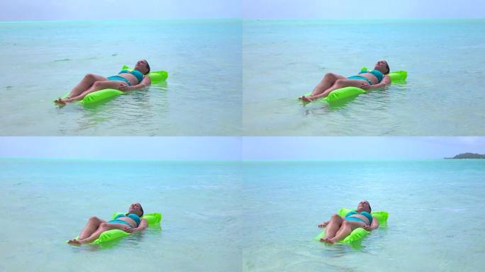 特写: 放松的年轻女子躺在异国情调的岛屿波拉波拉的充气水上床上