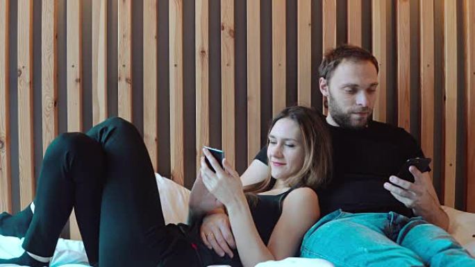 智能手机躺在地板上的年轻夫妇。男人和女人用小工具消磨时间，互相交谈