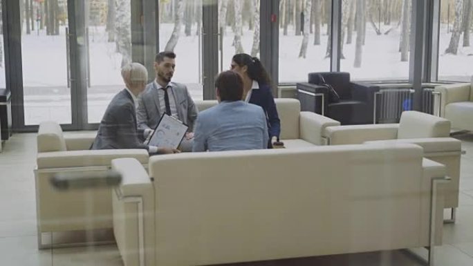 从电梯下移到一群商务人士的观点同事坐在现代商务中心大厅的沙发上讨论财务图表