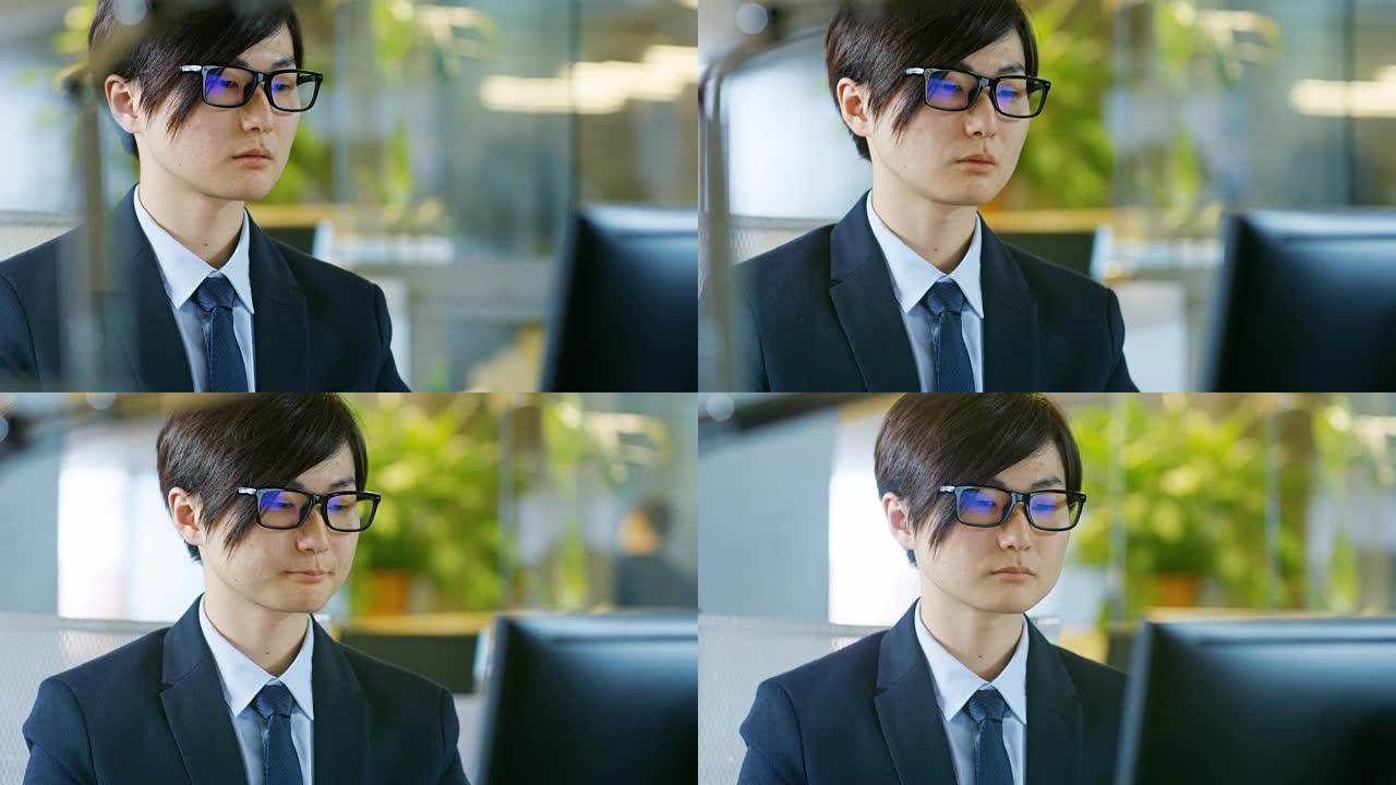 日本商人戴着眼镜，坐在办公桌前，在个人电脑上工作的肖像。