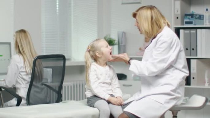 女医生做一个小女孩的喉咙检查。护士在后台工作。