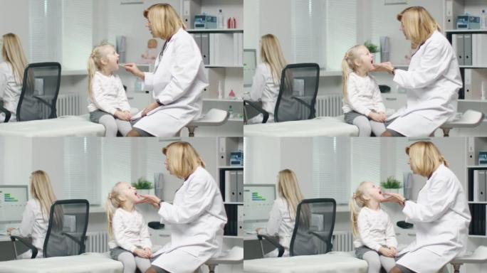 女医生做一个小女孩的喉咙检查。护士在后台工作。