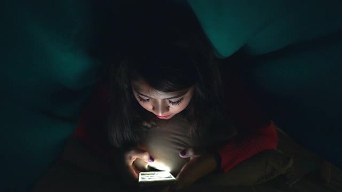 年轻女孩或青少年晚上在床上检查手机或与某人聊天。