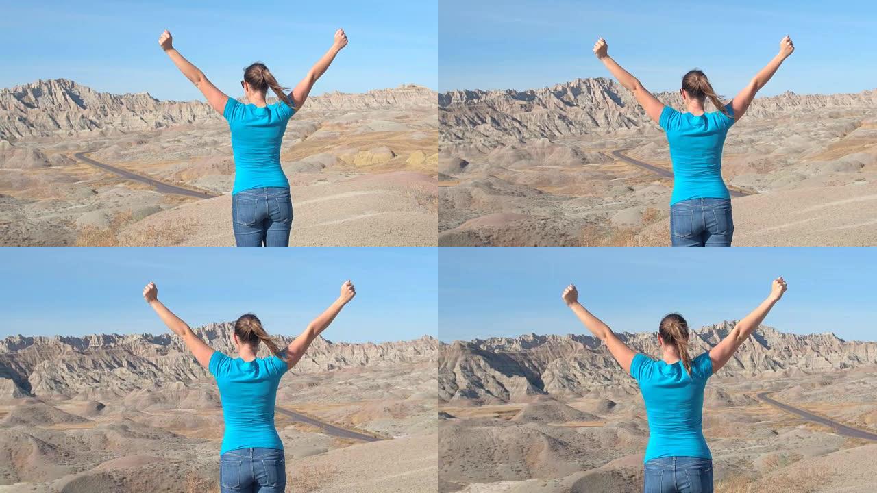 特写幸福的女人旅行者向荒地山顶的天空举起手臂