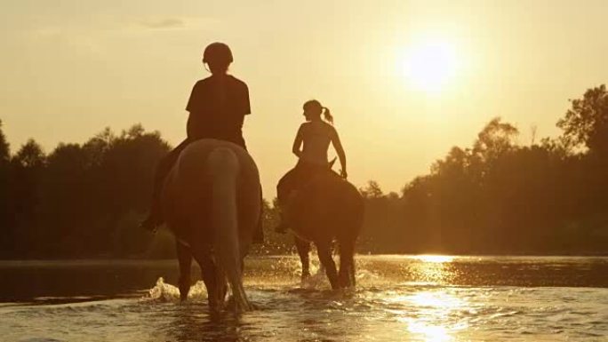 特写: 两个女孩在神奇的日落时沿河骑马