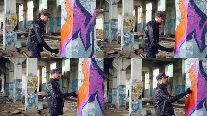 英俊的大胡子涂鸦艺术家正在废弃的建筑里喷漆。现代街头艺术、青年亚文化和创意人物概念。
