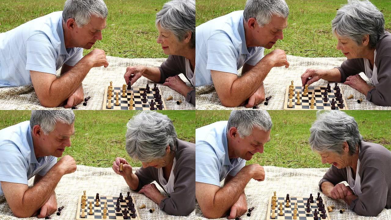 高级夫妇在公园里放松，躺在毯子上下棋