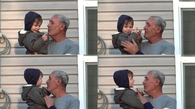 祖父和孙子说话，微笑，玩得开心，看着户外相机。老人手握小男孩。4K