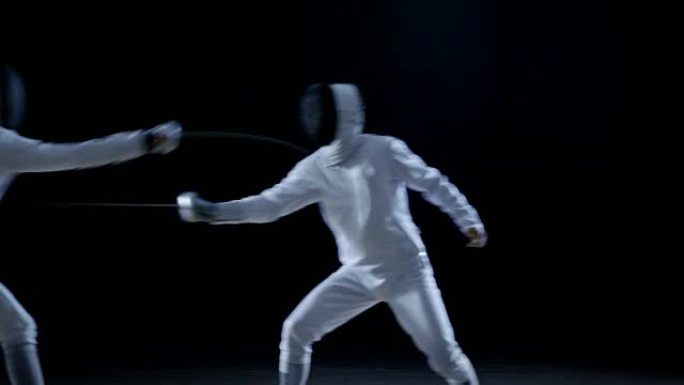 两名专业击剑手在花剑搏斗中表现出精湛的剑术。他们跳跃、推力和弓步。拍摄孤立在黑色背景上。