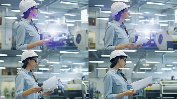美丽的黑发工业工程师戴着安全帽，在穿过工厂时研究蓝图和文件。