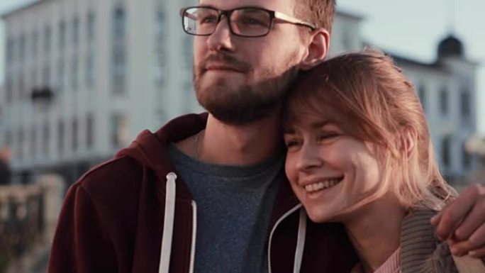 年轻美丽的夫妇站在市中心，向一边看的肖像。快乐的男人和女人在日落时拥抱