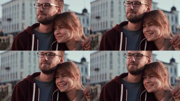 年轻美丽的夫妇站在市中心，向一边看的肖像。快乐的男人和女人在日落时拥抱