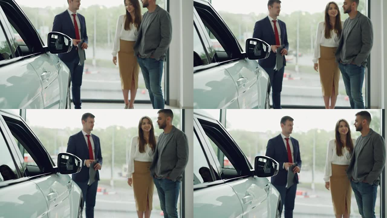 夫妻俩一起选择了他们的第一辆车，并在车展上与自信的销售人员交谈，幸福的女人在微笑和倾听。专注于闪亮的