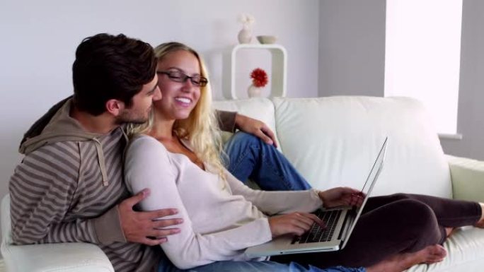 快乐的年轻夫妇坐在沙发上使用笔记本电脑
