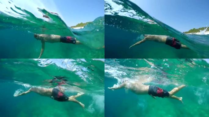 水下: 活跃的年轻人在海洋中游泳，背景是岩石海滩