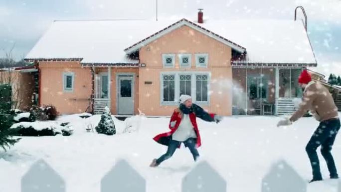 年轻美丽的夫妇在下雪时互相扔雪球。快乐的男人和女人在他们田园诗般的房子的院子里玩雪。享受冬天的家庭。
