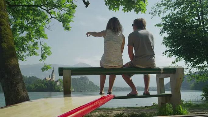 年轻夫妇坐在湖边的长凳上，拿着SUP板