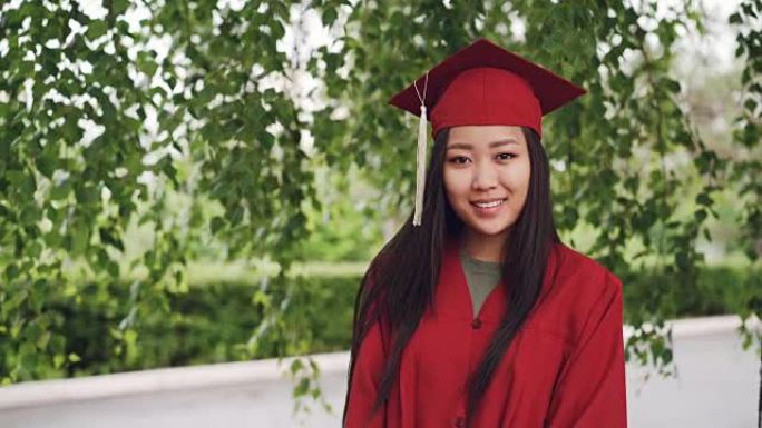 迷人的亚洲女孩的肖像成功毕业的学生穿着礼服和灰浆板站在校园里，微笑着看着相机。青年与教育理念。