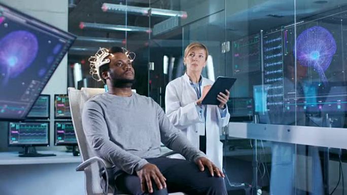 戴着脑电波扫描耳机的男人坐在椅子上，而科学家则用平板电脑监督过程。在现代的大脑研究实验室监视器显示脑