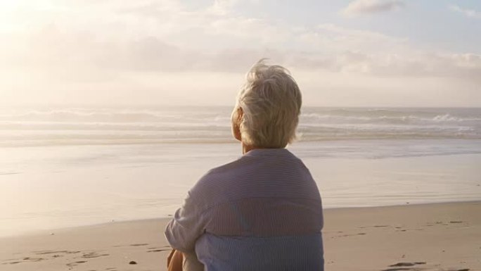 老女人在海滩上看太阳在海洋上落下的后视图