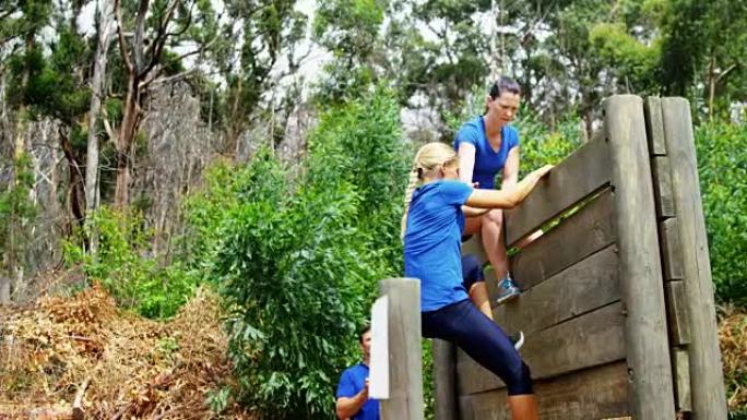 女教练协助健康女性在障碍路线4k时爬过木墙