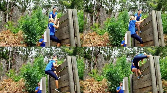 女教练协助健康女性在障碍路线4k时爬过木墙