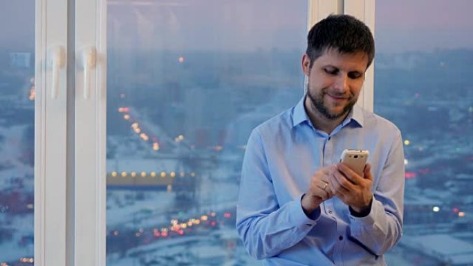 男人在晚上站在窗前使用智能手机