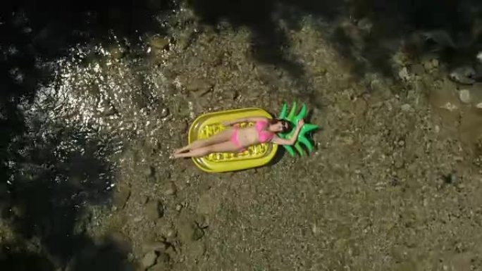 空中: 年轻的游客在菠萝形漂浮物上沐浴着太阳