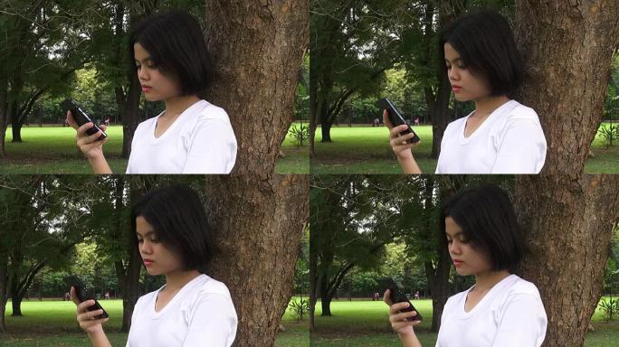高清格式:美丽的年轻潮女使用智能手机在秋季公园。穿着秋装的漂亮年轻女子在手机上发短信。