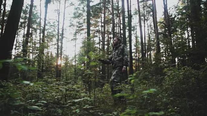 身穿迷彩服的年轻人站在森林里环顾四周。探索大自然领土的猎人男性