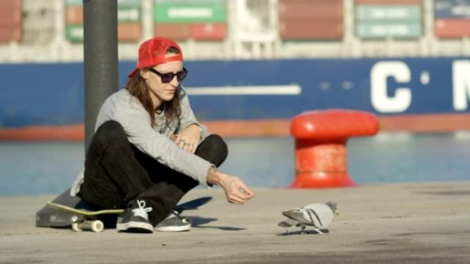 特写: 滑板手在滑冰休息时坐在滑板上喂鸽子