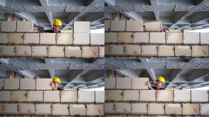 中年建筑工人建造一堵墙，并在上面放混凝土砖