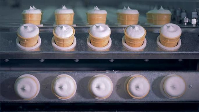 将一排排带有冰淇淋的威化饼杯插入工业机器中，然后提起