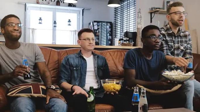 非裔美国男性朋友在电视上观看体育节目。多民族极客迷集中在爆米花的沙发上