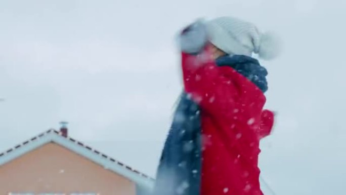美丽的年轻微笑的女人在飘落的雪中旋转。穿着红色外套和围巾的女孩在院子里享受冬日。