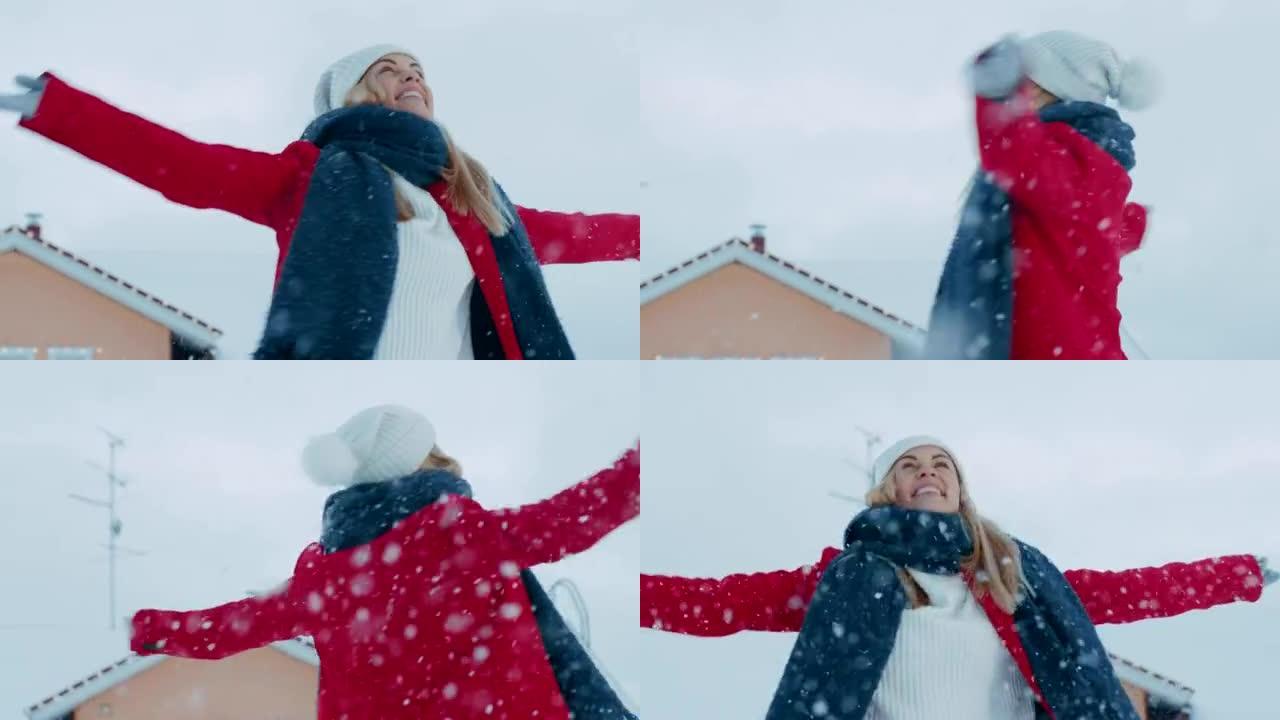 美丽的年轻微笑的女人在飘落的雪中旋转。穿着红色外套和围巾的女孩在院子里享受冬日。